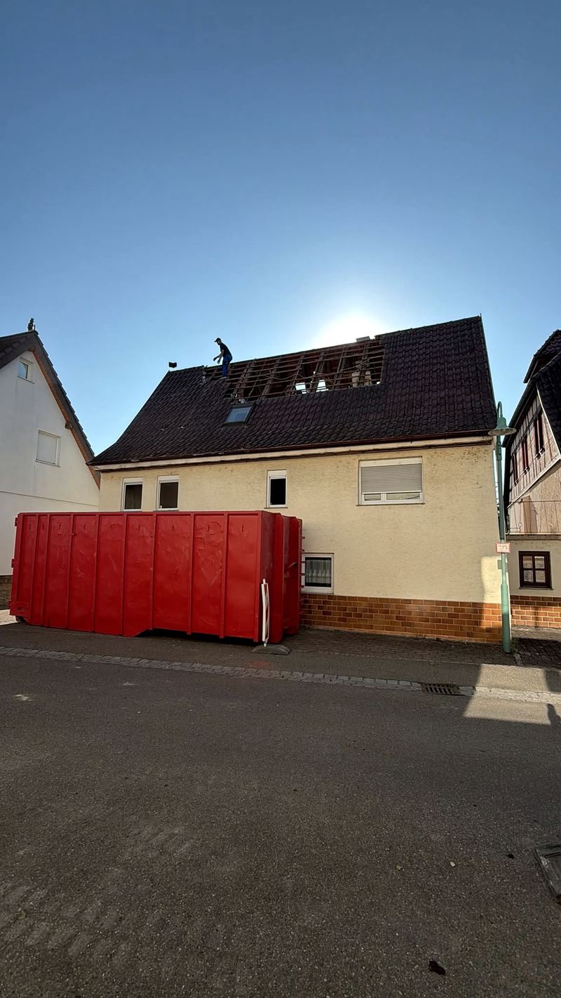 Wohnhaus mit geoeffnetem Dachstuhl, davor ein roter Abrollcontainer